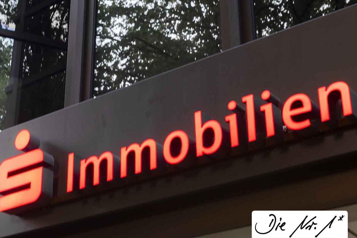 Außenaufnahme eines Gebäudeeingangs mit der Leuchtschrift: S Immobilien; sowie einer handschriftlichen Notiz am Bildrand: Die Nummer 1*